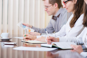 Besprechung am Tisch Drei Menschen sitzen in einer Besprechung am Tisch.